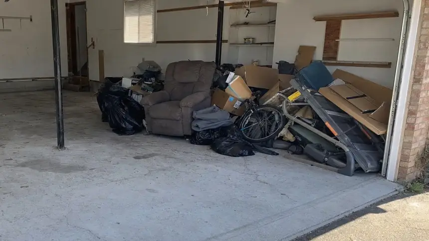 A two-car garage half cleared, with an old recliner, boxes, a bike and a treadmill stacked on one side