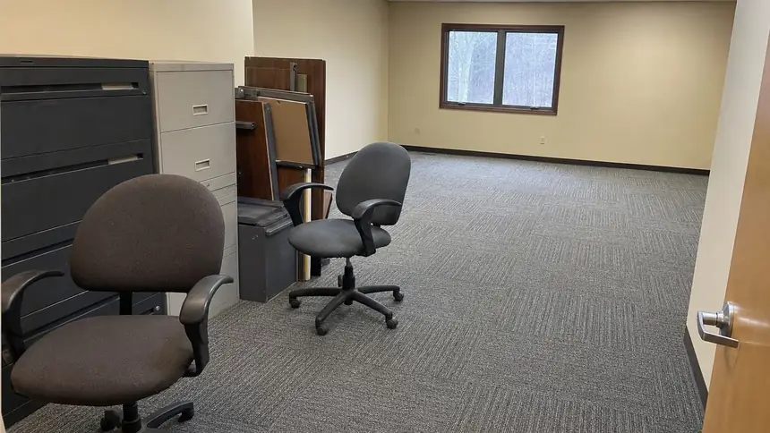 An office being cleared out, with chairs, filing cabinets and desk parts stacked by the door